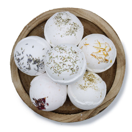 White bath bombs with visible ingredients in a wooden bowl on a white background