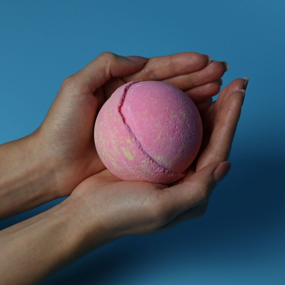 Pink bath bomb held in hands against a blue background