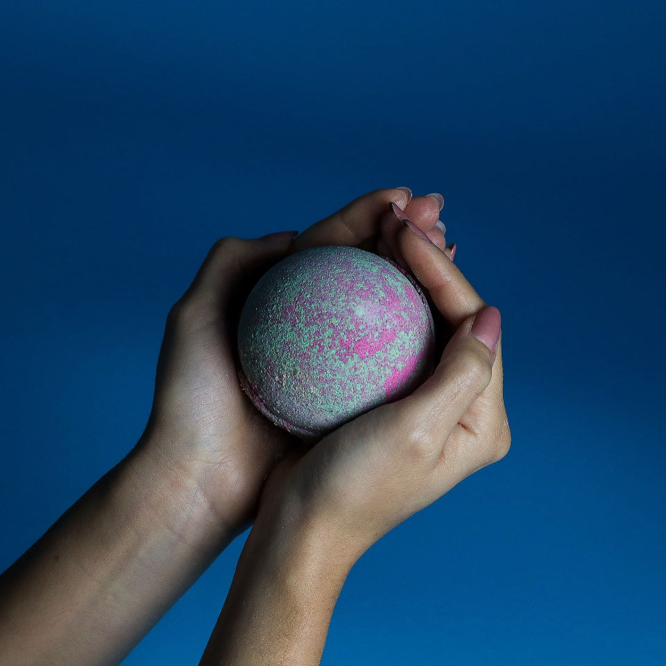 Hands holding a colorful bath bomb against a blue background
